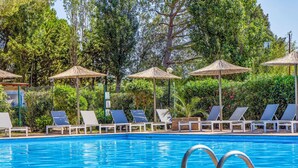 A swimming pool with lounge chairs and umbrellas, surrounded by greenery. - Bungalow Superior by Interhome (Capalbio)
