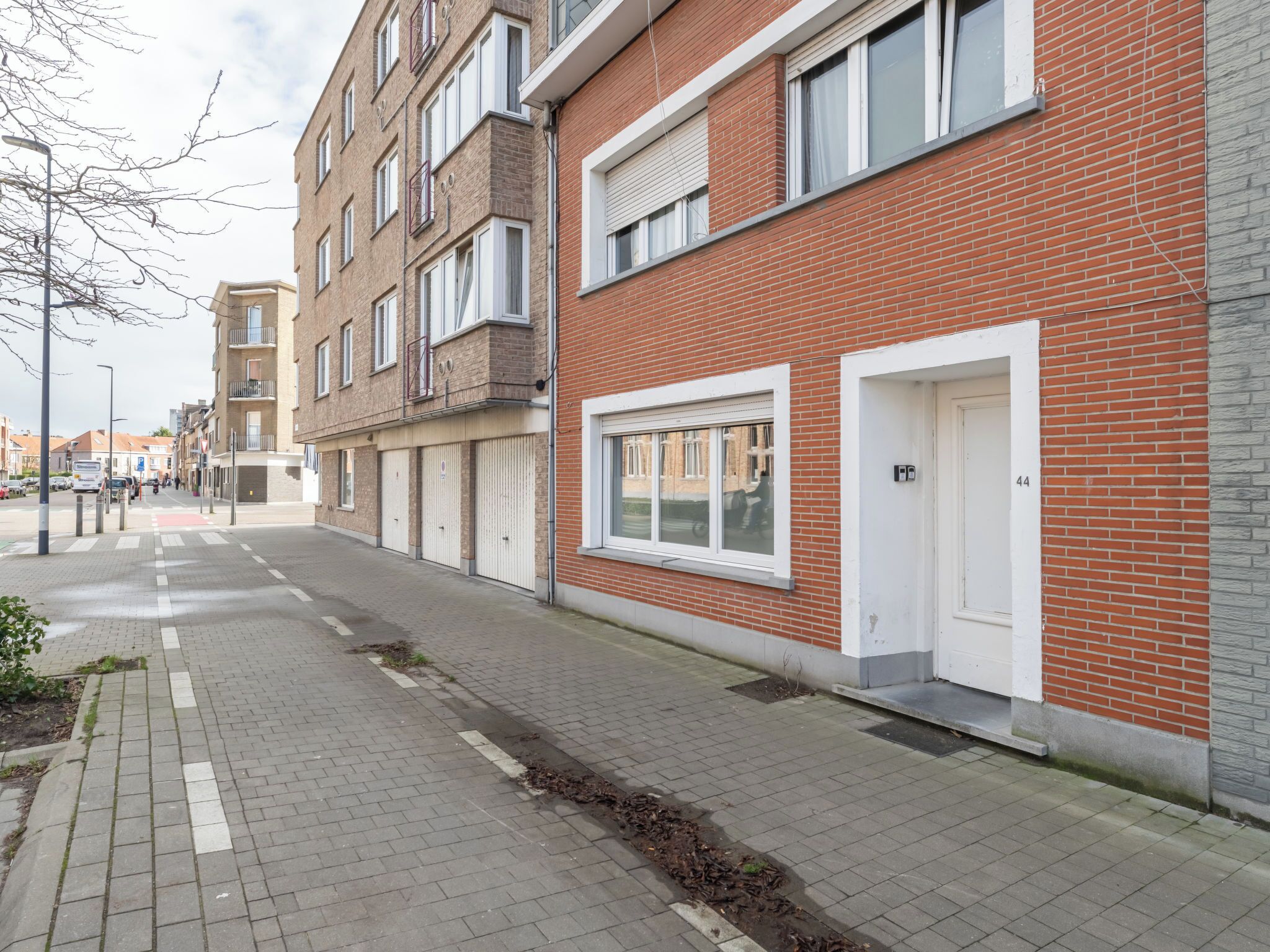 Una hilera de edificios de apartamentos de ladrillo rojo con puertas y ventanas blancas, un paseo pavimentado y un cielo despejado.