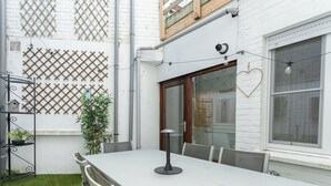 Een witte tafel met stoelen in een kamer met witte bakstenen muren, een houten deur en een raam met een hartvormige decoratie.