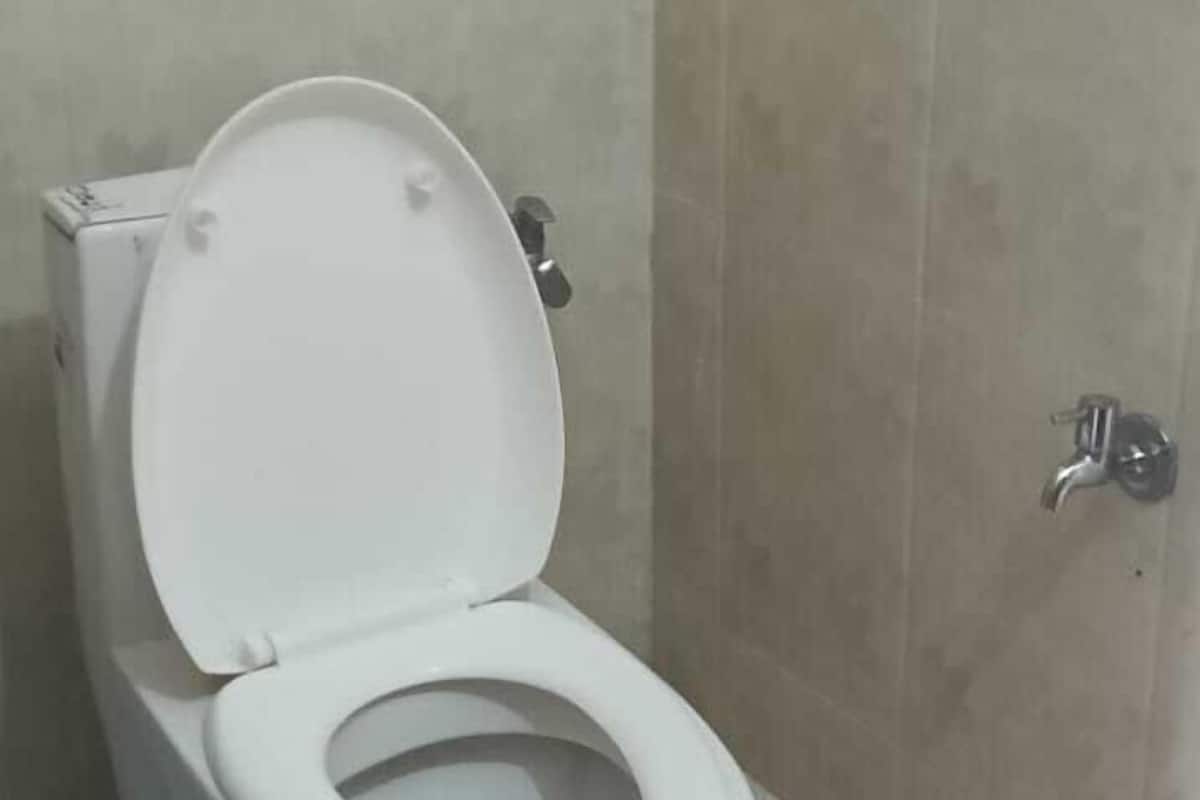 Une salle de bain avec des toilettes blanches, un seau bleu et un mur carrelé.