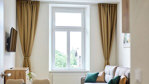A modern living room with a sofa, dining table, chairs, and a large window with curtains. - Residence 44 (Prague)