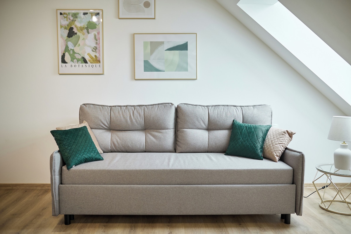 A modern living room with a grey sofa, two cushions, and a small side table with a lamp.
