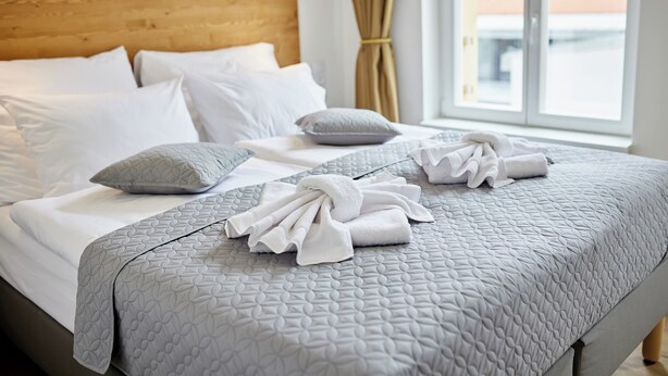 A neatly made bed with white and gray bedding, a wooden headboard, and a view of buildings through a window. - Residence 44 (Prague)