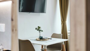 A modern dining area with a flat-screen TV mounted on the wall, a table with chairs, and a potted plant. - Residence 44 (Prague)