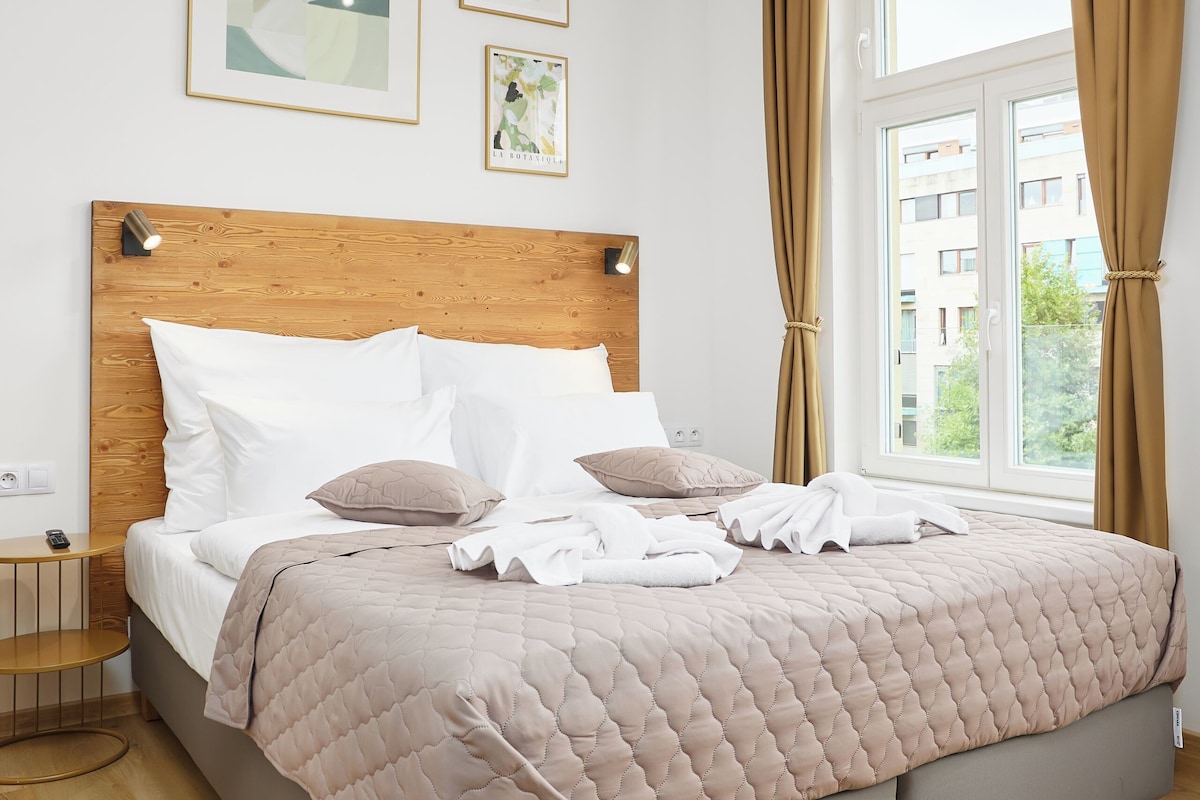 A neatly made bed with a wooden headboard, a bedside table, and a window with curtains.