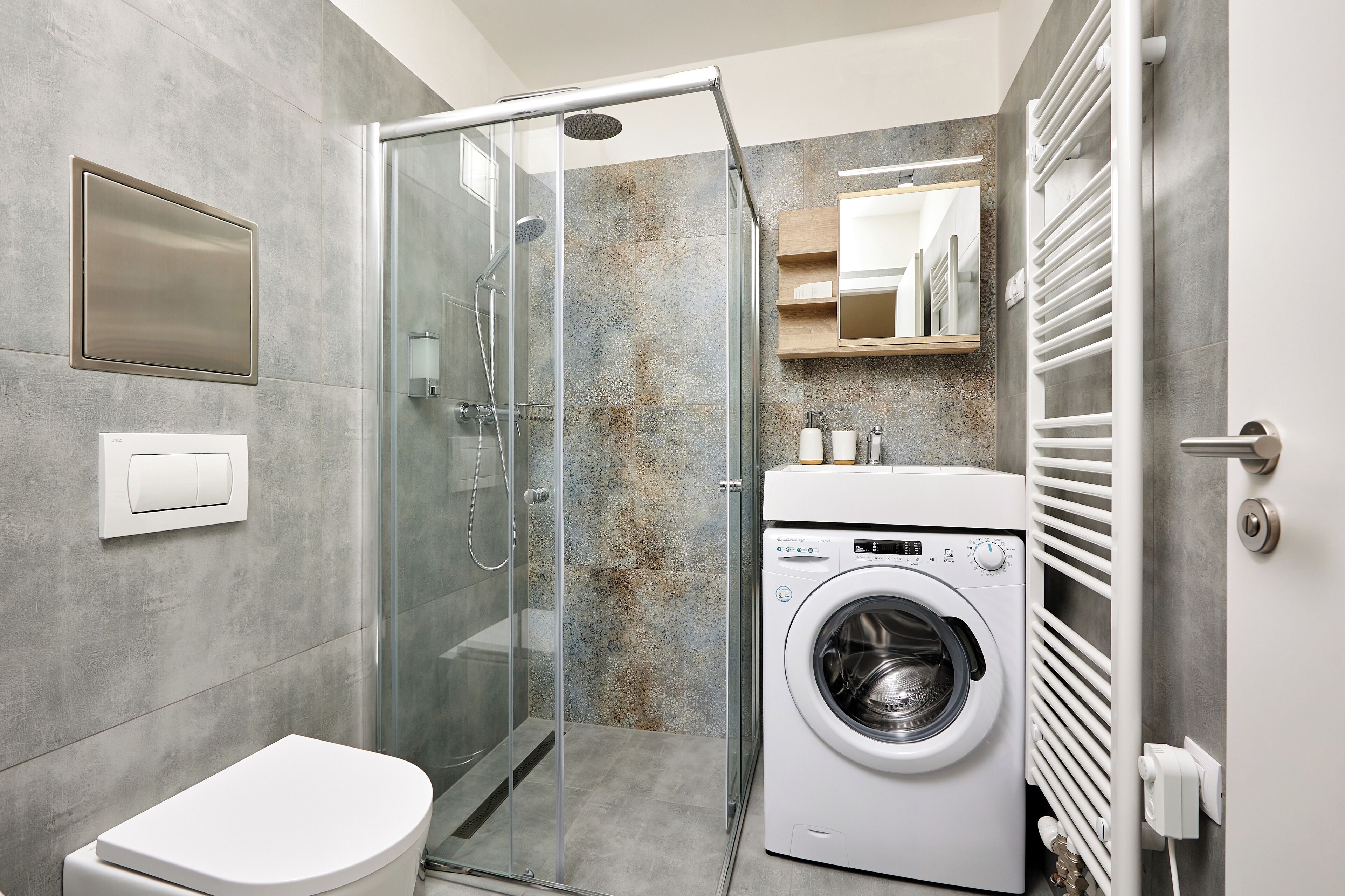 A modern bathroom with a glass shower enclosure, a built-in washing machine, and a toilet.
