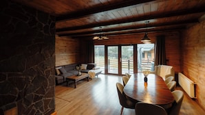 Une pièce spacieuse avec un plafond en bois, un mur en pierre et une grande table à manger entourée de chaises.