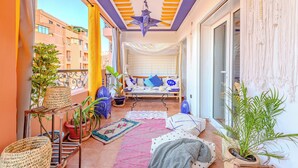 A balcony with potted plants, a woven shelf, a patterned rug, and a bed with pillows and a hanging light fixture. - Boho chic retreat (Marrakech)