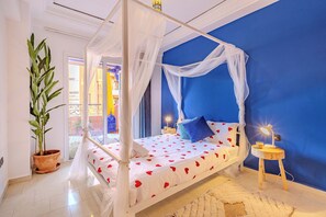 Ein Schlafzimmer mit Himmelbett, einem Blumentopf, einem Nachttisch mit Lampe und Blick ins Freie.