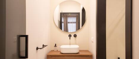 Un baño con tocador de madera, espejo redondo y lavamanos blanco.