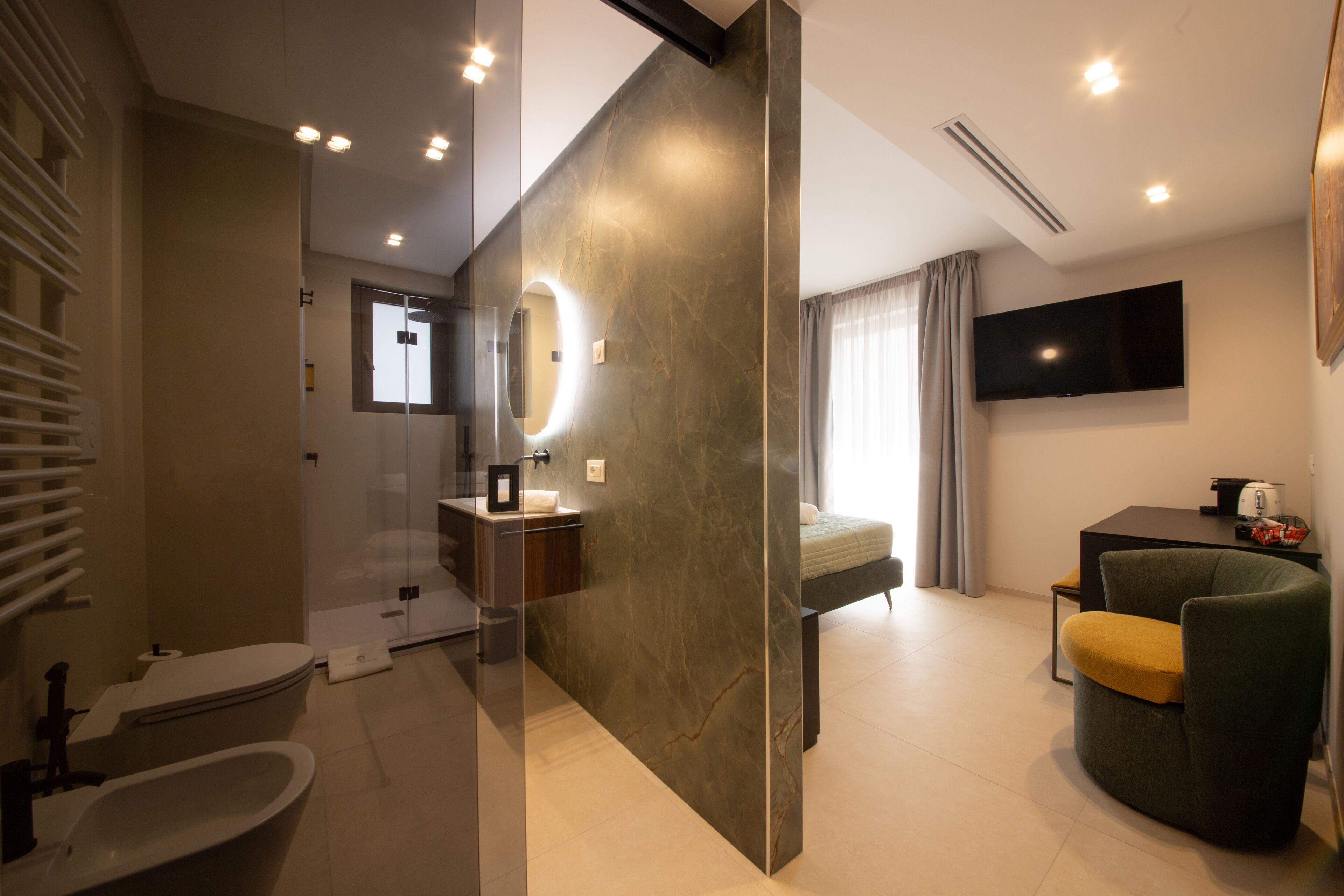 A modern hotel room with a bathroom, a bed, a TV, and a seating area.
