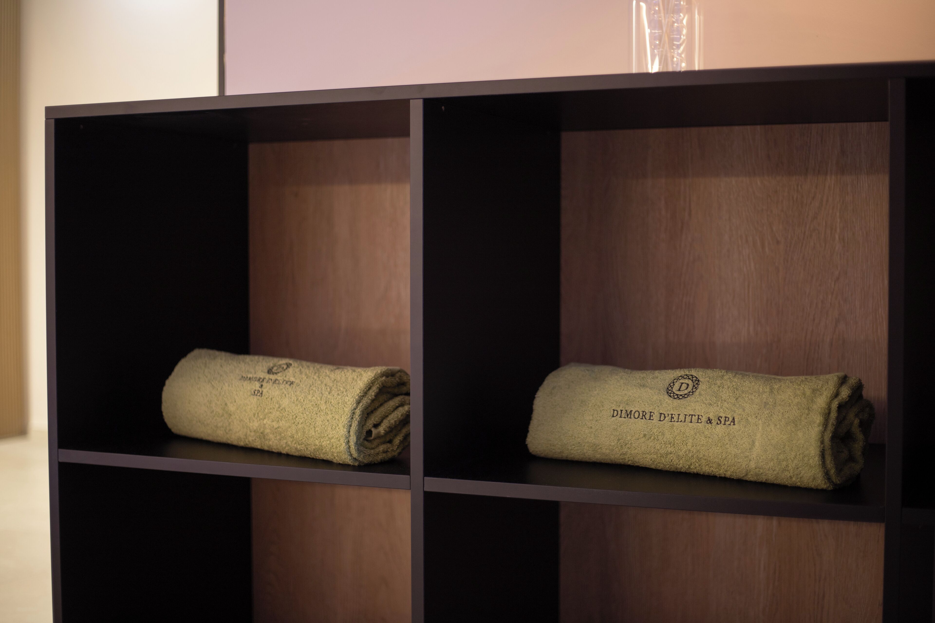 Two neatly folded towels on a shelf with the text "DIMORE D'ELITE & SPA" visible on them.