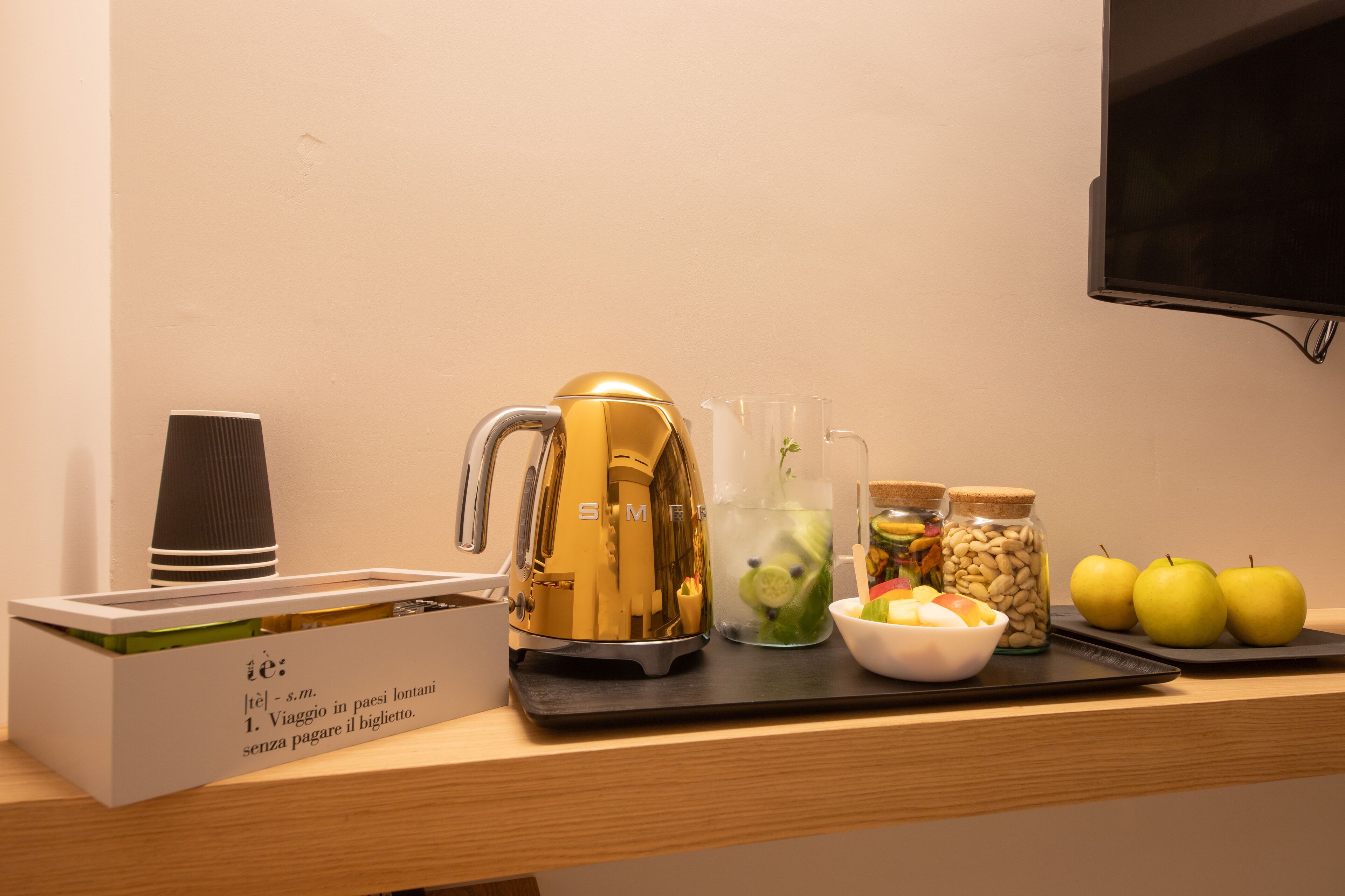 A breakfast setup with a coffee maker, a coffee cup, a fruit bowl, and a tray with apples and nuts.