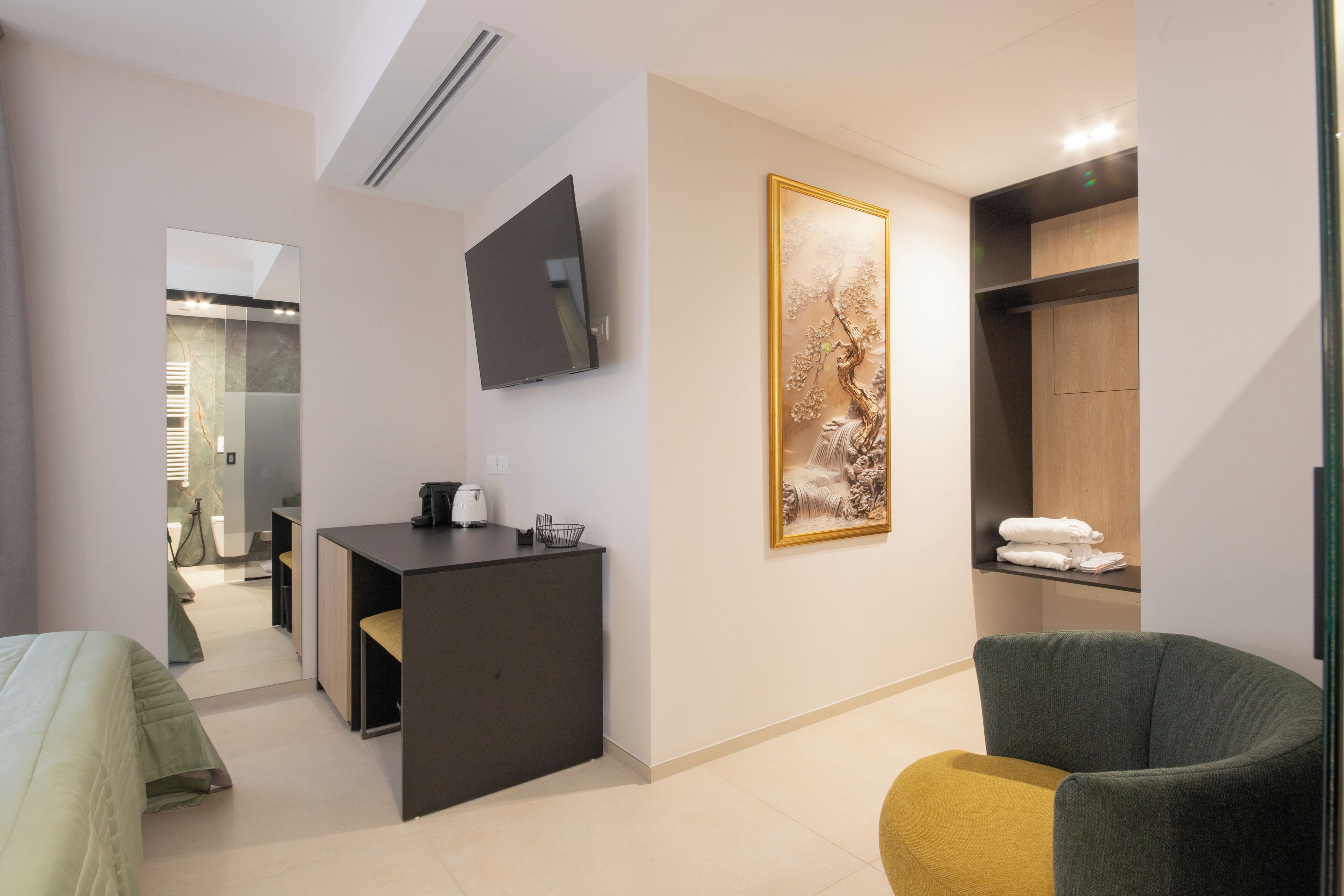 A modern hotel room with a bed, a desk, a chair, a TV, and a painting on the wall.