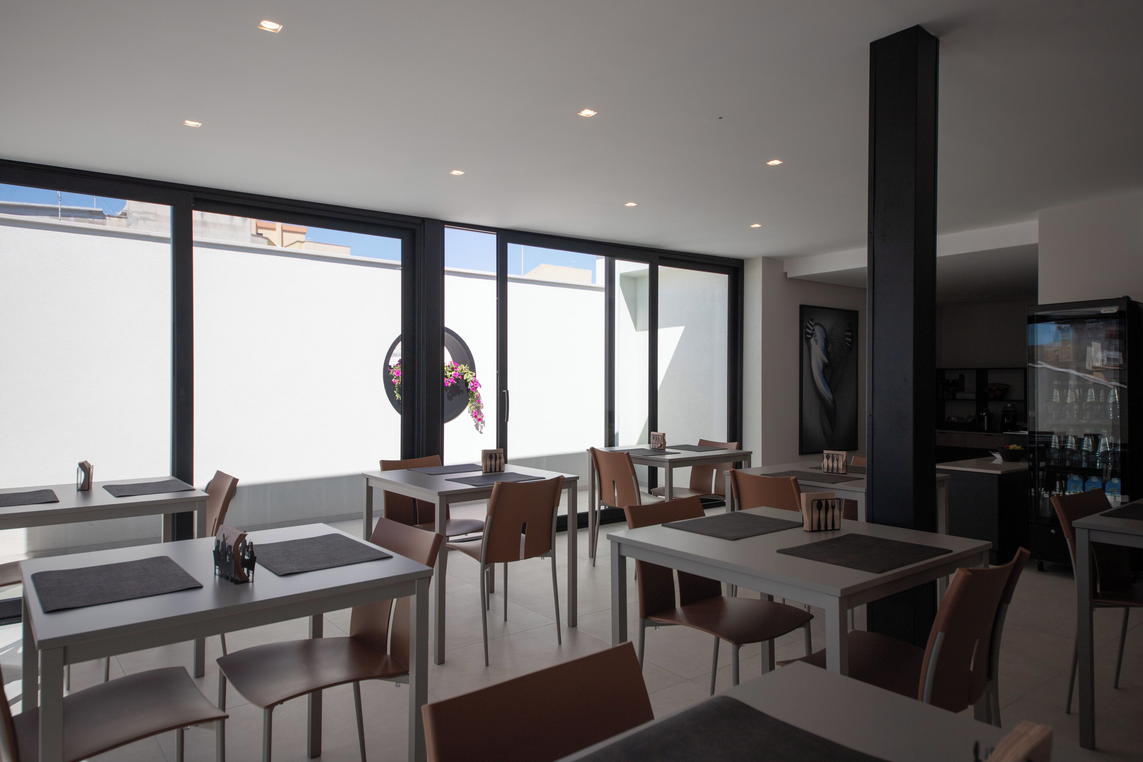 Een moderne eethoek met tafels en stoelen, grote ramen en een zichtbare keuken in de achtergrond.