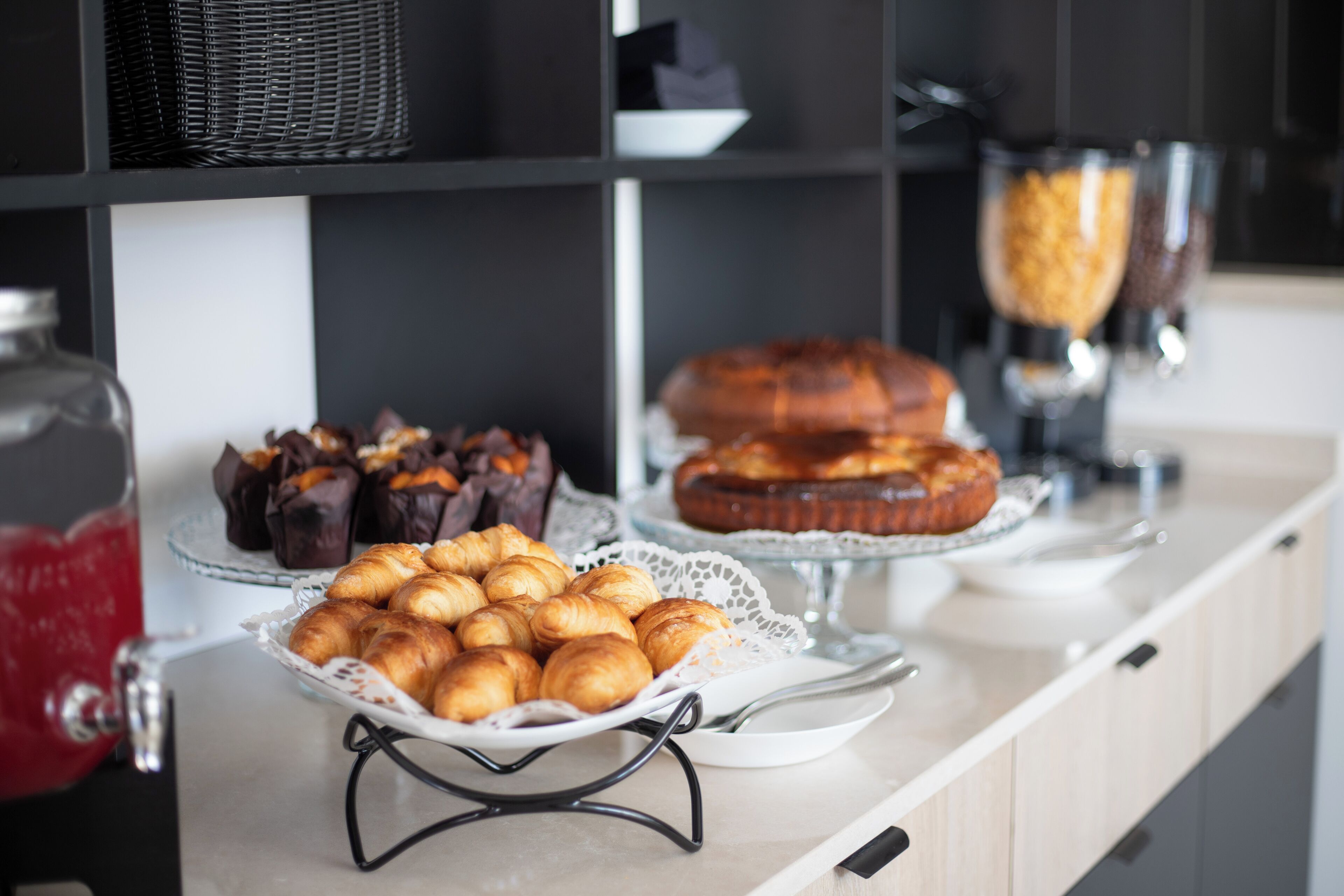 Una mesa de bufé con diversos productos horneados, incluyendo croissants, bollería con cobertura de chocolate y una barra de pan.