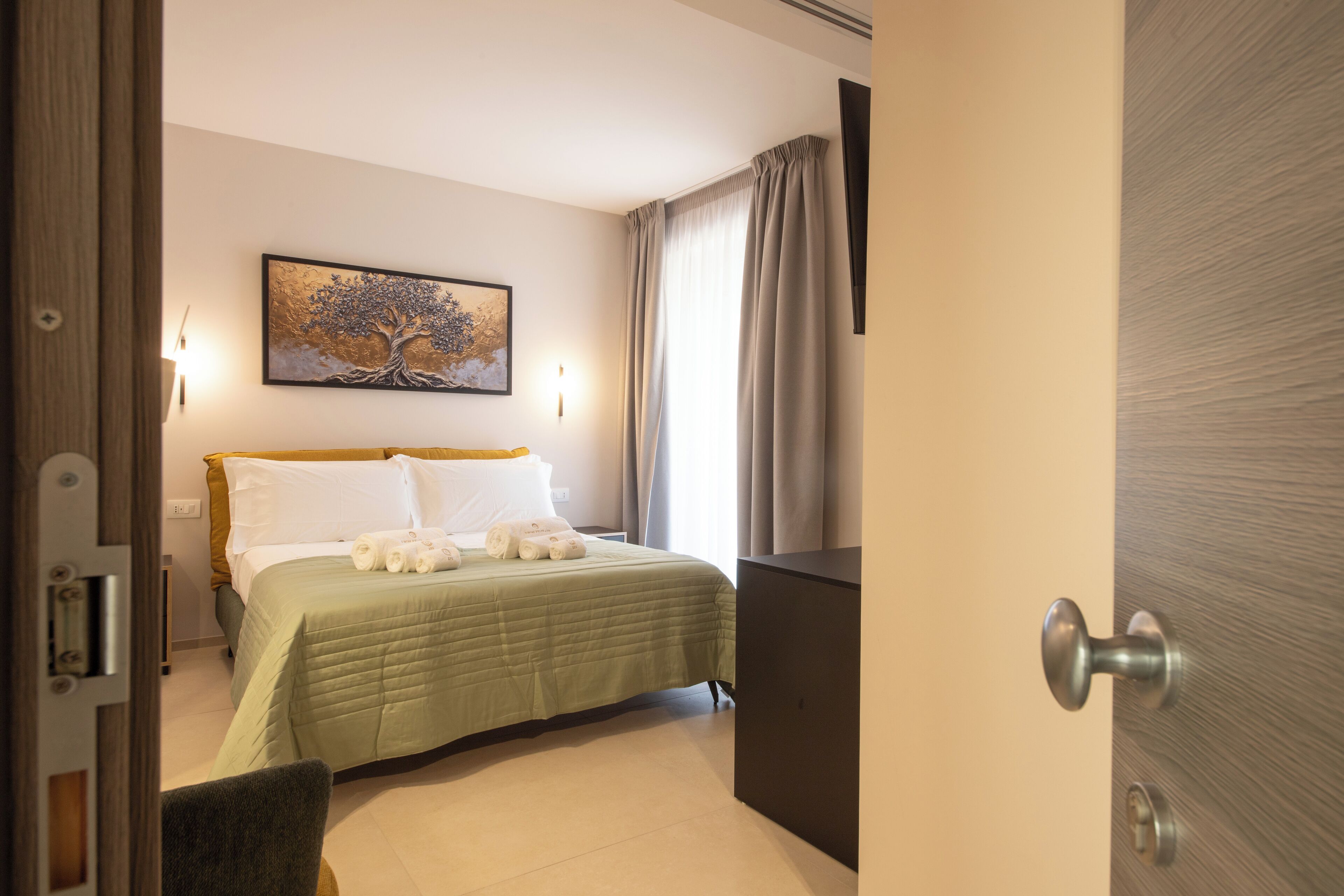 A hotel room with a bed, a painting on the wall, a door, and a light fixture.