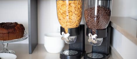 Two coffee dispensers with different beverages, a cake on a stand, and a white bowl.