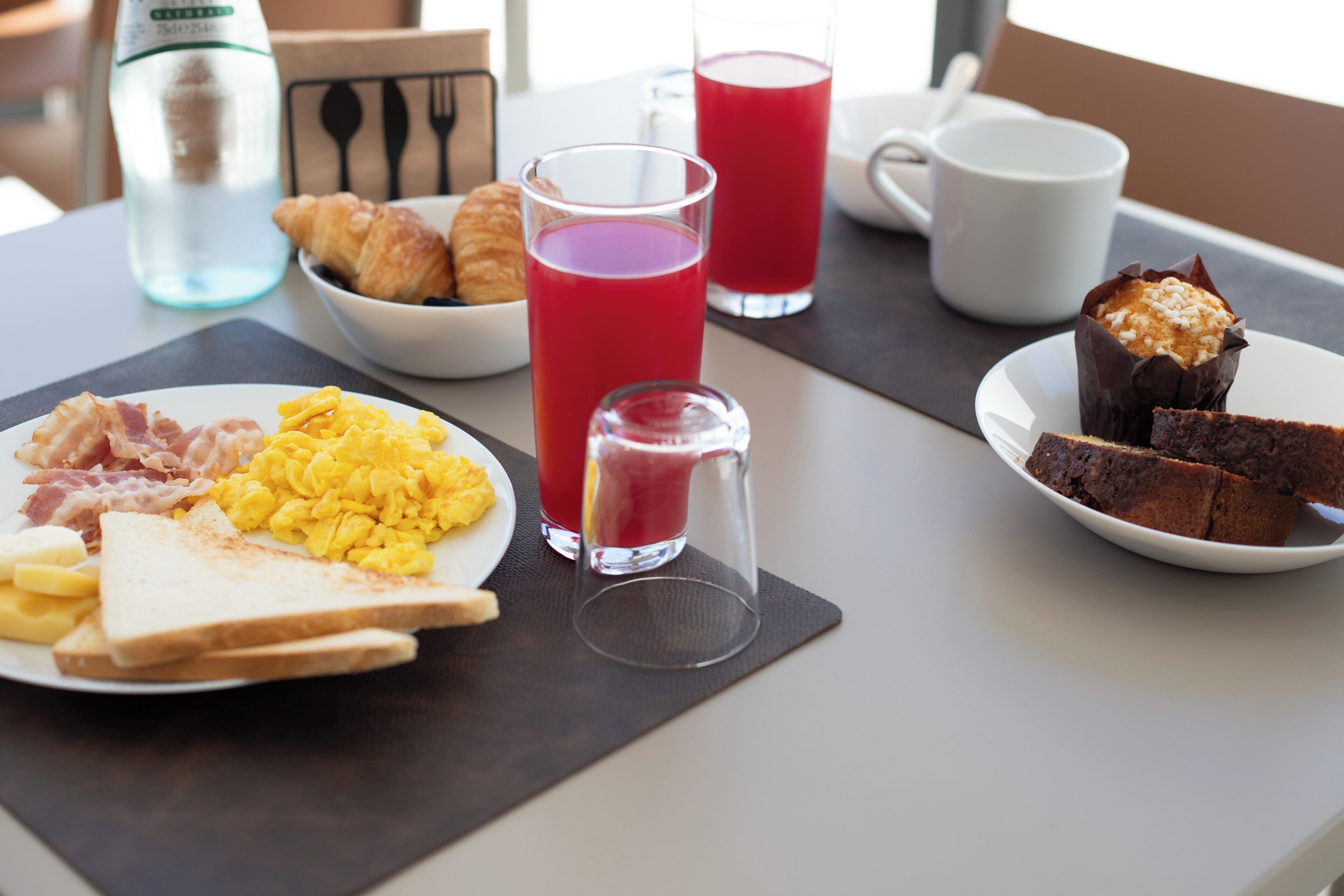 Una mesa de desayuno con cruasanes, huevos revueltos, tostadas y un muffin.