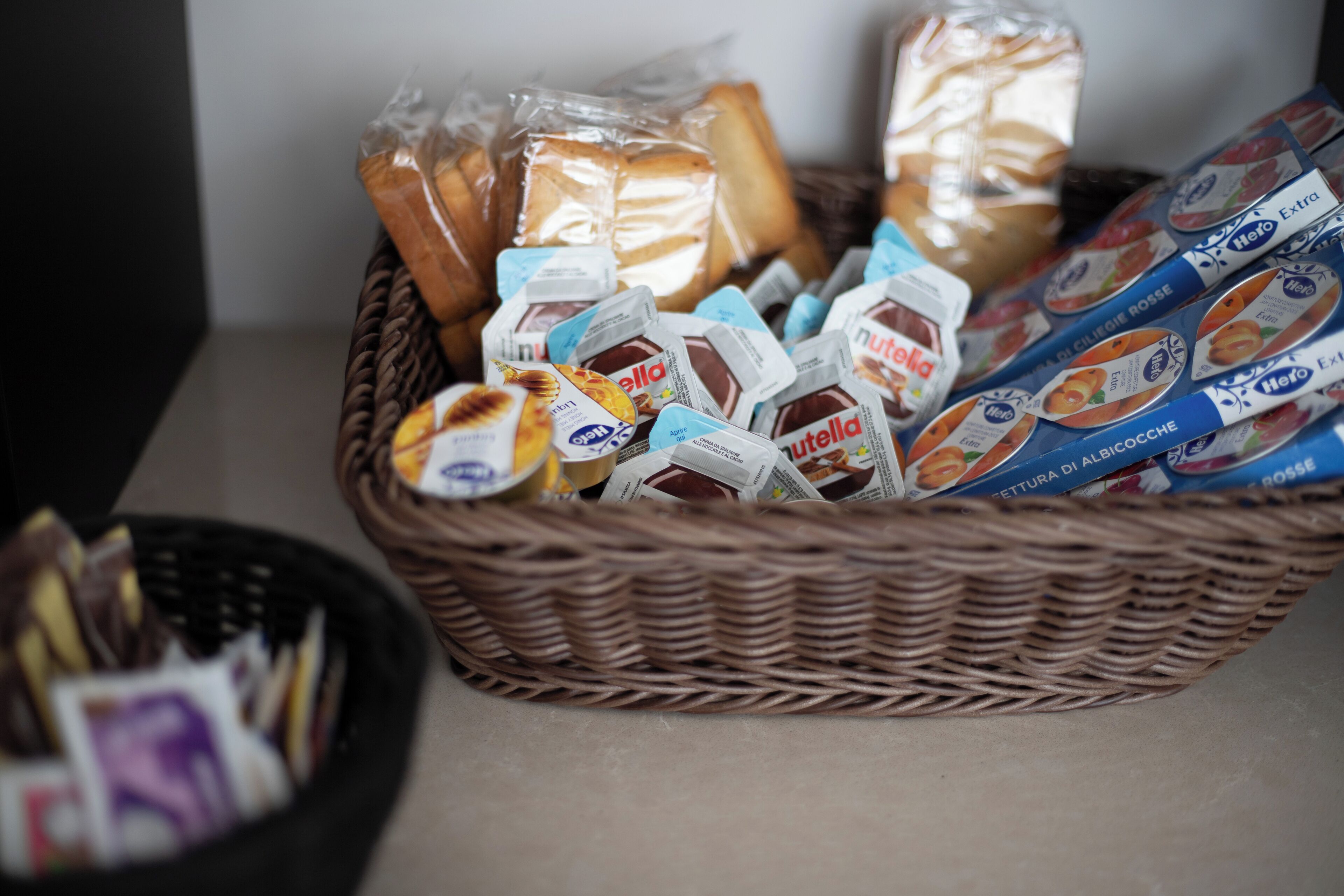Un panier en osier rempli de divers produits alimentaires, notamment du pain et des pots de Nutella.