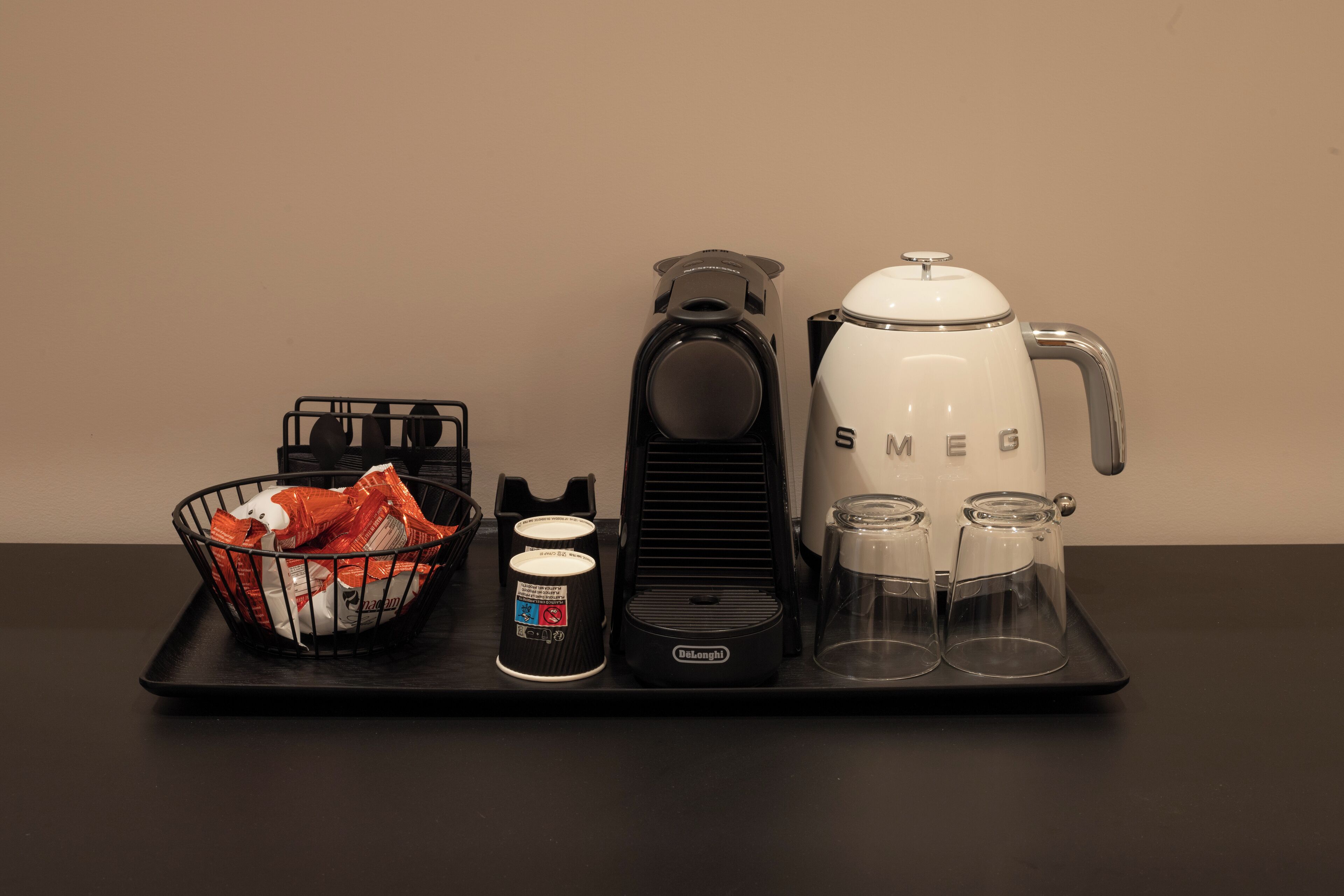 A coffee station with a coffee maker, cups, and a basket of coffee pods.