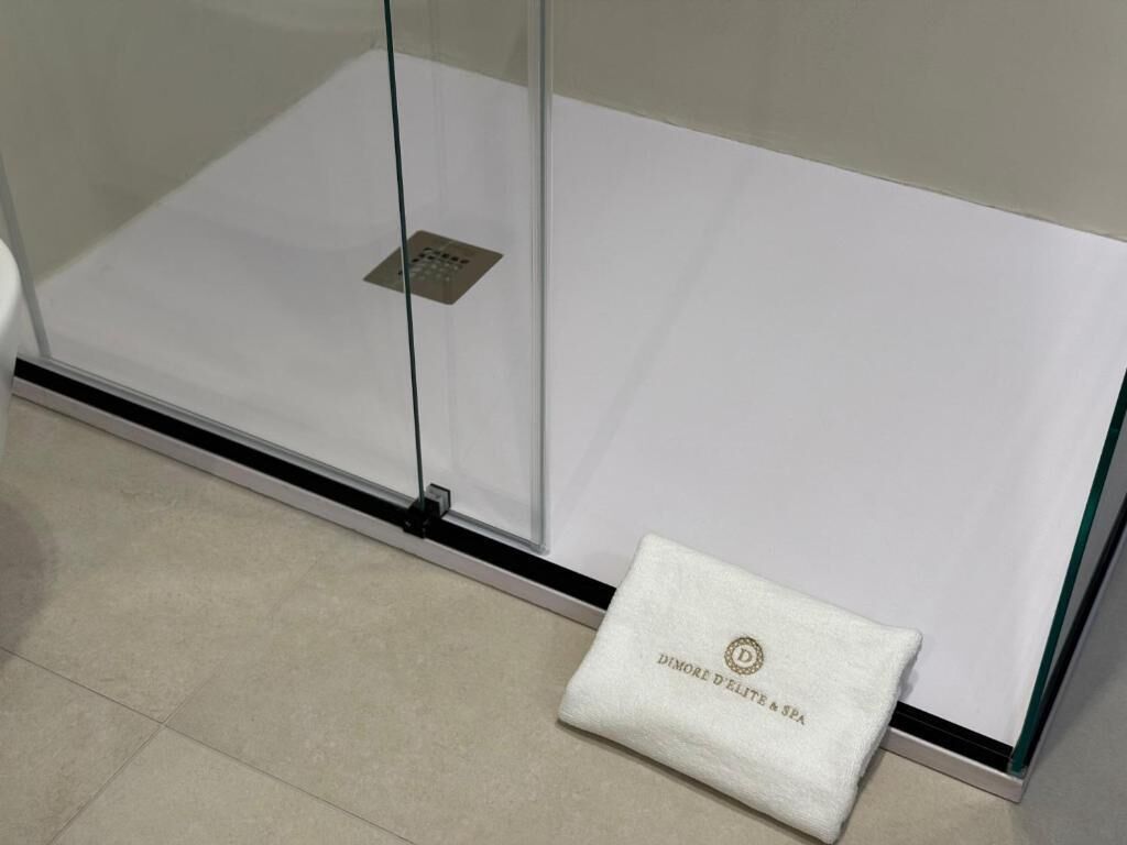 A glass shower enclosure with a control panel and a towel with "Dimore D'Elite & Spa" branding.