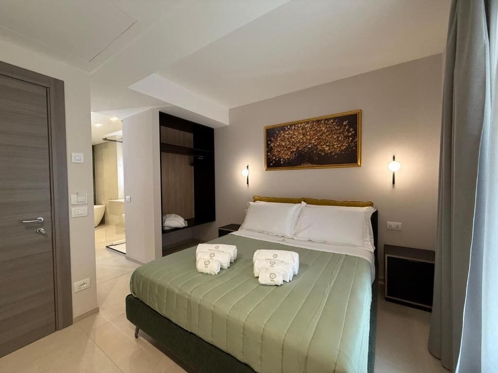 A hotel room with a bed, a painting on the wall, and a door to the left.