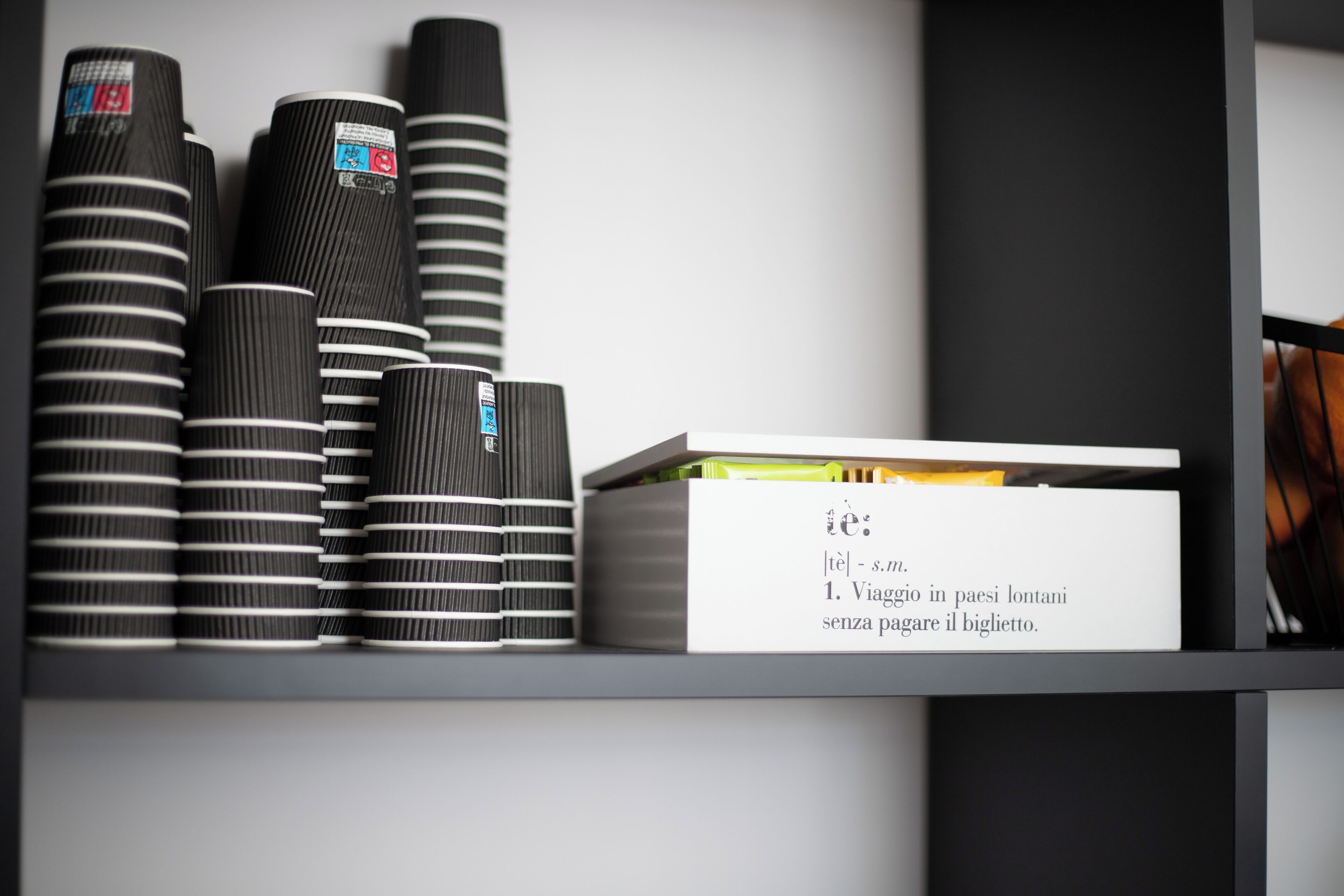Una repisa con tazas a rayas negras y blancas y una caja blanca con texto.