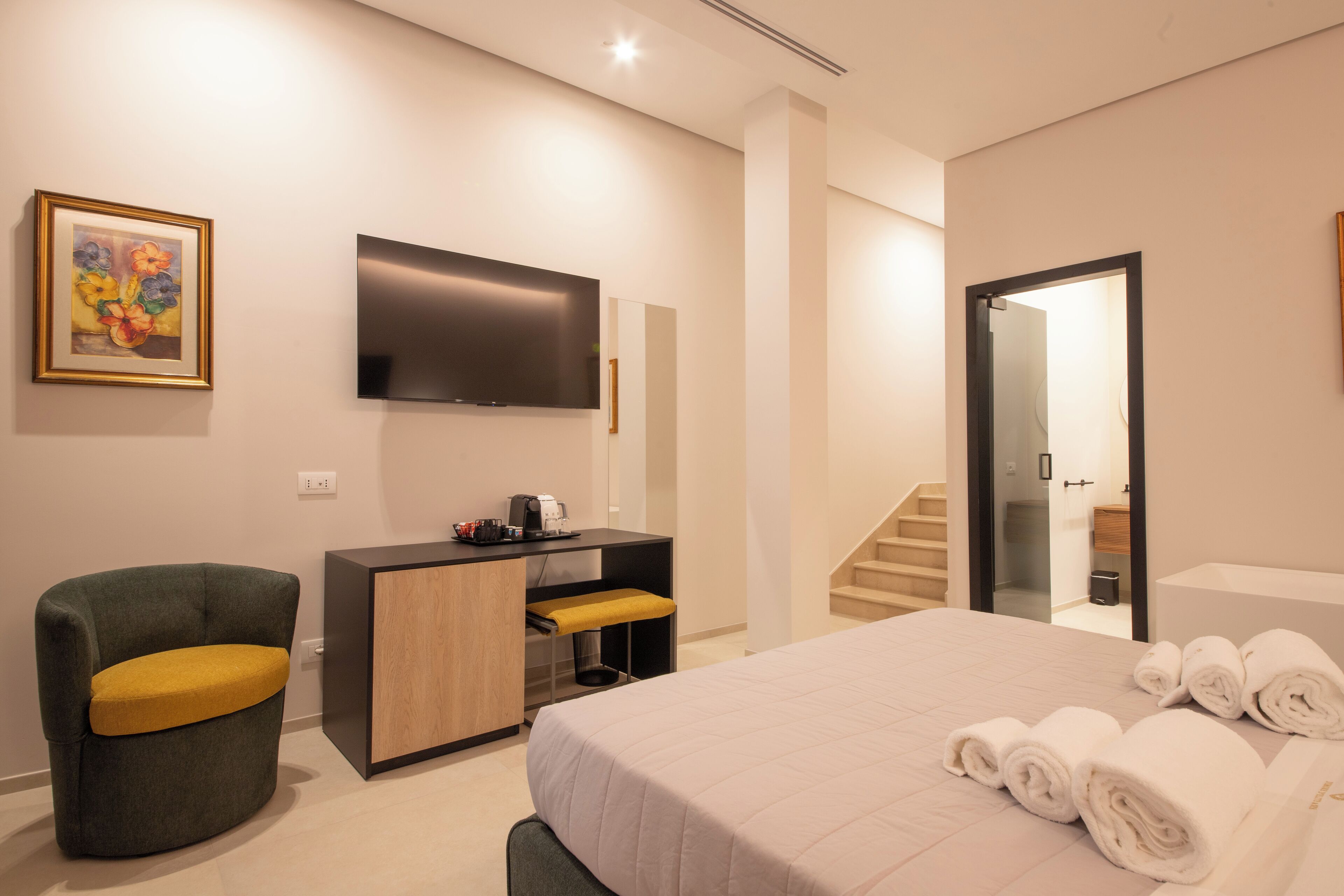 Una habitación de hotel moderna con una cama, un escritorio con silla, un televisor de pantalla plana y un cuadro en la pared.
