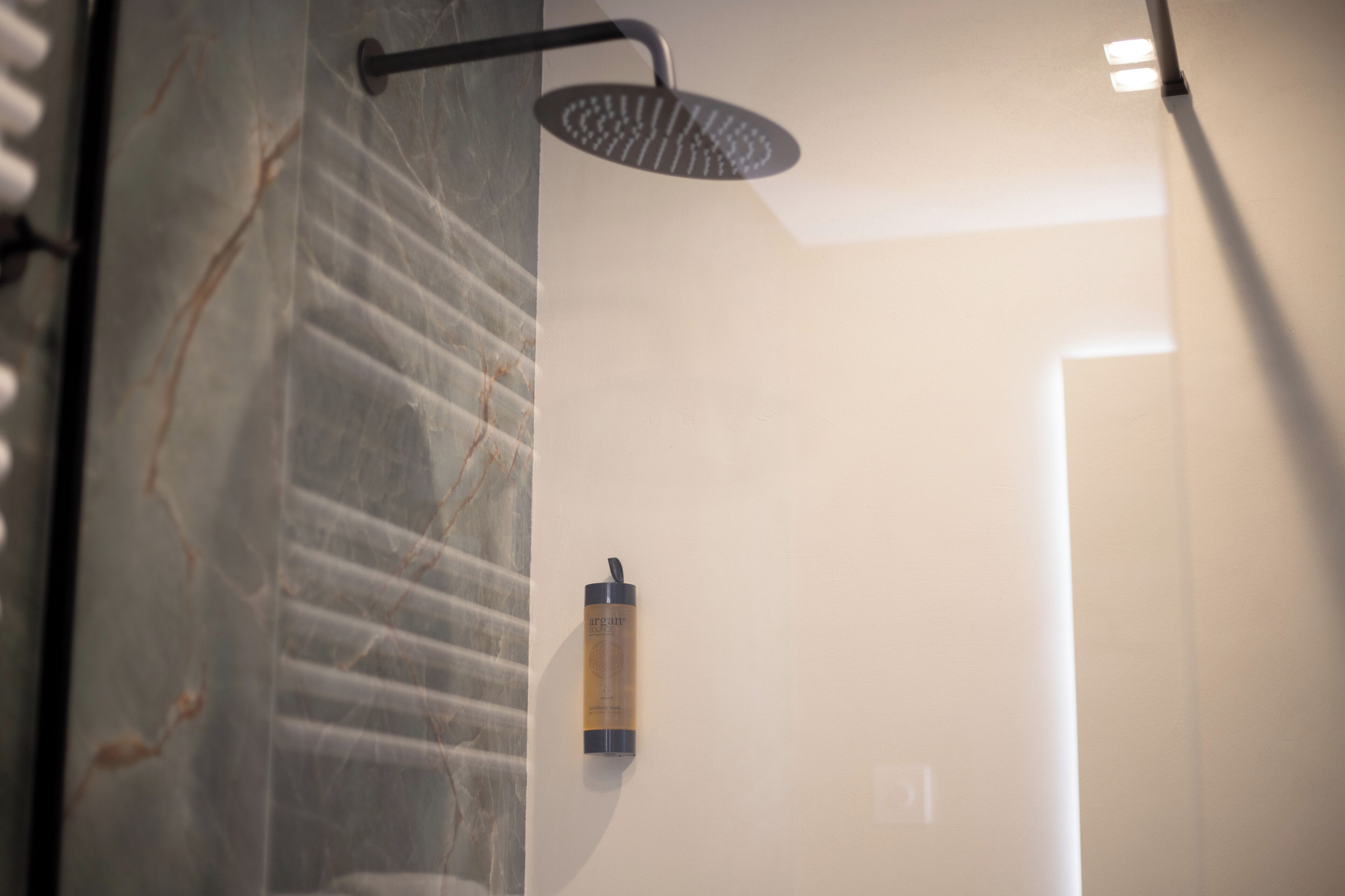 Ducha con cabezal de ducha tipo lluvia, una botella de champú y pared de mármol.