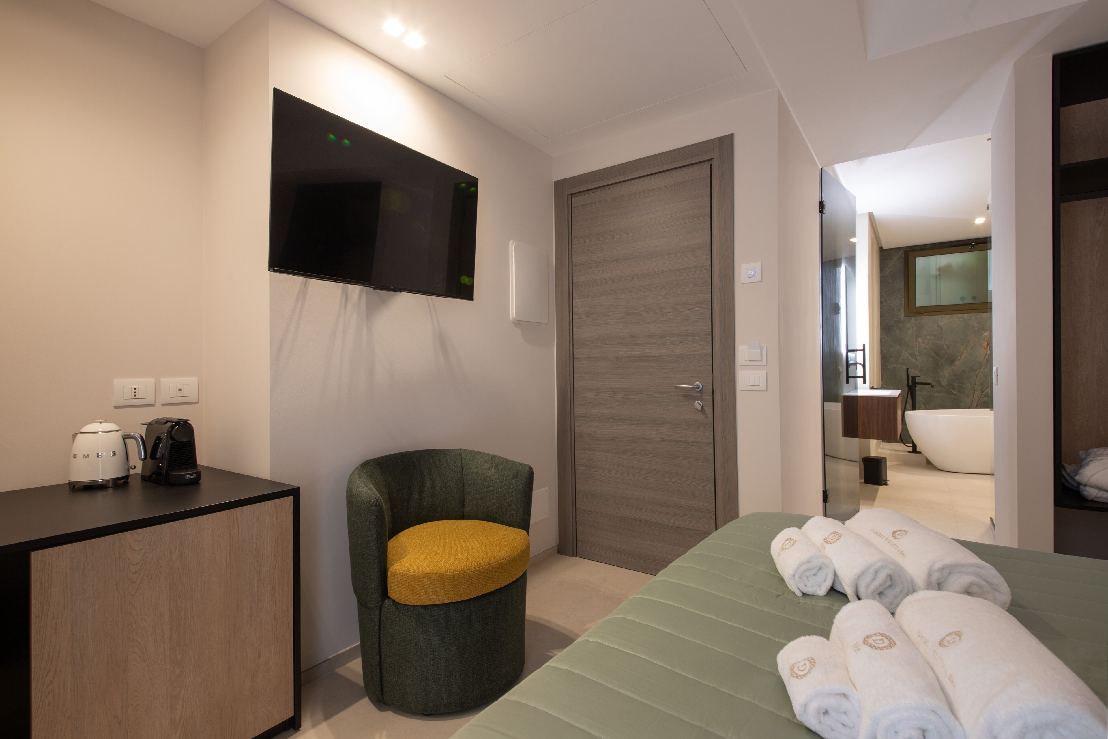 A hotel room with a bed, a desk with a coffee maker, a TV mounted on the wall, and a door leading to a bathroom with a bathtub.