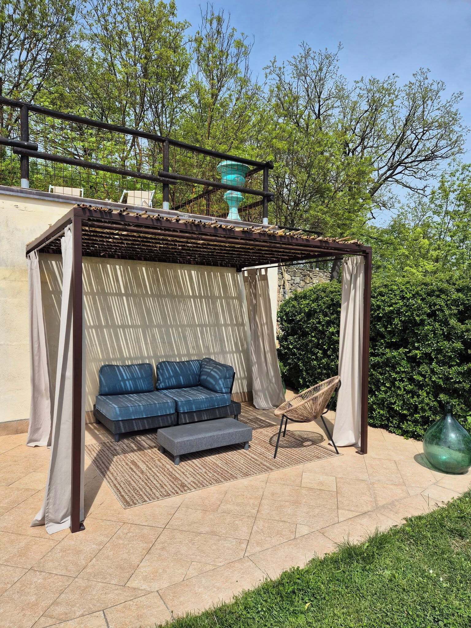 Un espacio de estar al aire libre cubierto con un sofá y cojines, una silla colgante y un jarrón decorativo.