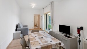 Een moderne kamer met een eettafel, een grijze bank, een televisie en een raam met gordijnen.