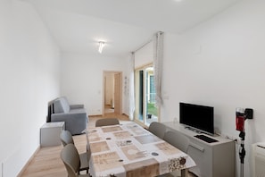 Una habitación moderna con una mesa de comedor, un sofá gris, televisor y una ventana con cortinas.