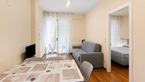 Uma sala moderna com um sofá, uma mesa de jantar com toalha de mesa estampada e uma televisão.