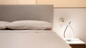 Cama com almofadas, mesa de cabeceira com abajur e interruptor de luz na parede.