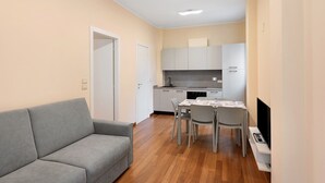 Um espaço de estar compacto com sofá, mesa de jantar, cadeiras, televisão e cozinha compacta.
