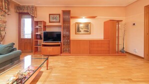 A living room with a television, wooden cabinets, a glass cabinet, and a painting on the wall.