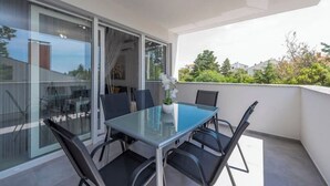 En balkong med ett glasbord och stolar, en krukväxt och utsikt över grönska och byggnader.