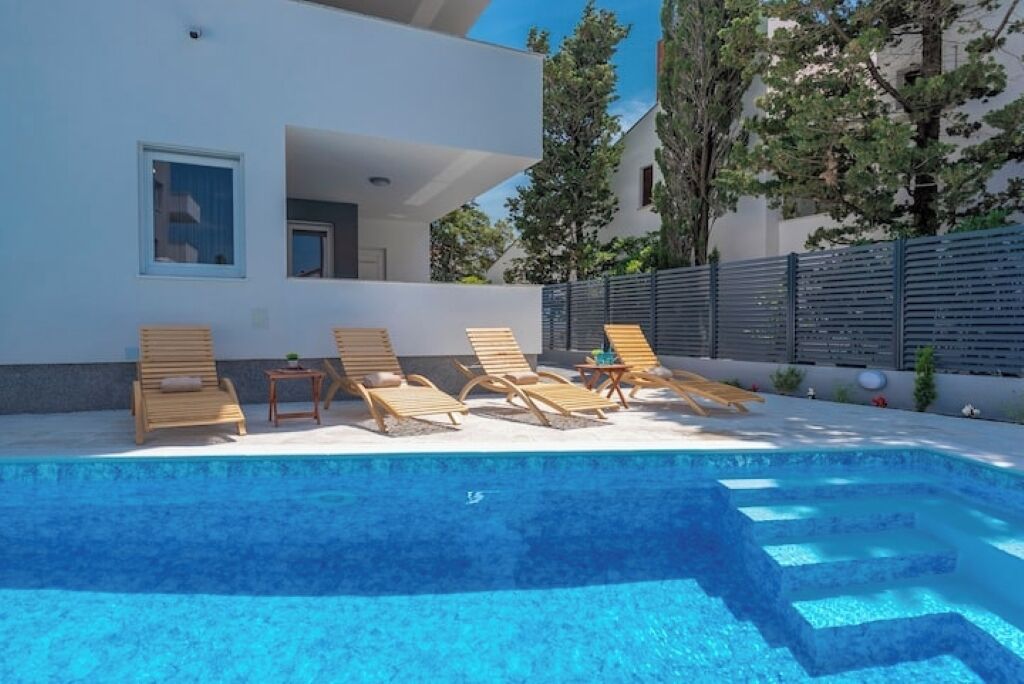 A modern outdoor swimming pool with wooden loungers and a small table.