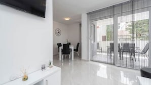 A modern living room with a flat-screen TV mounted on the wall, a dining area with a table and chairs, and a sliding glass door leading to an outdoor patio. - Villa Mel Mari 4 (Prelog)