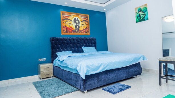 Ein Schlafzimmer mit blauer Wand, einem großen Bett, einem Nachttisch und einer Kommode.