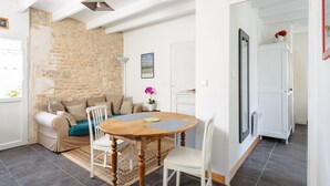 A cozy living room with a stone wall, a wooden dining table, and a sofa. - Charming Gîte "Les Jardins d'Harmonie" for 2 in Bourgneuf – Charente-Maritime (Bourgneuf)