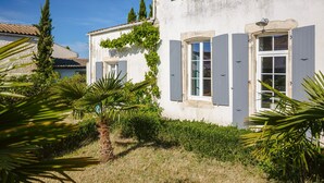A white building with shutters, a small garden with palm trees, and a clear blue sky.