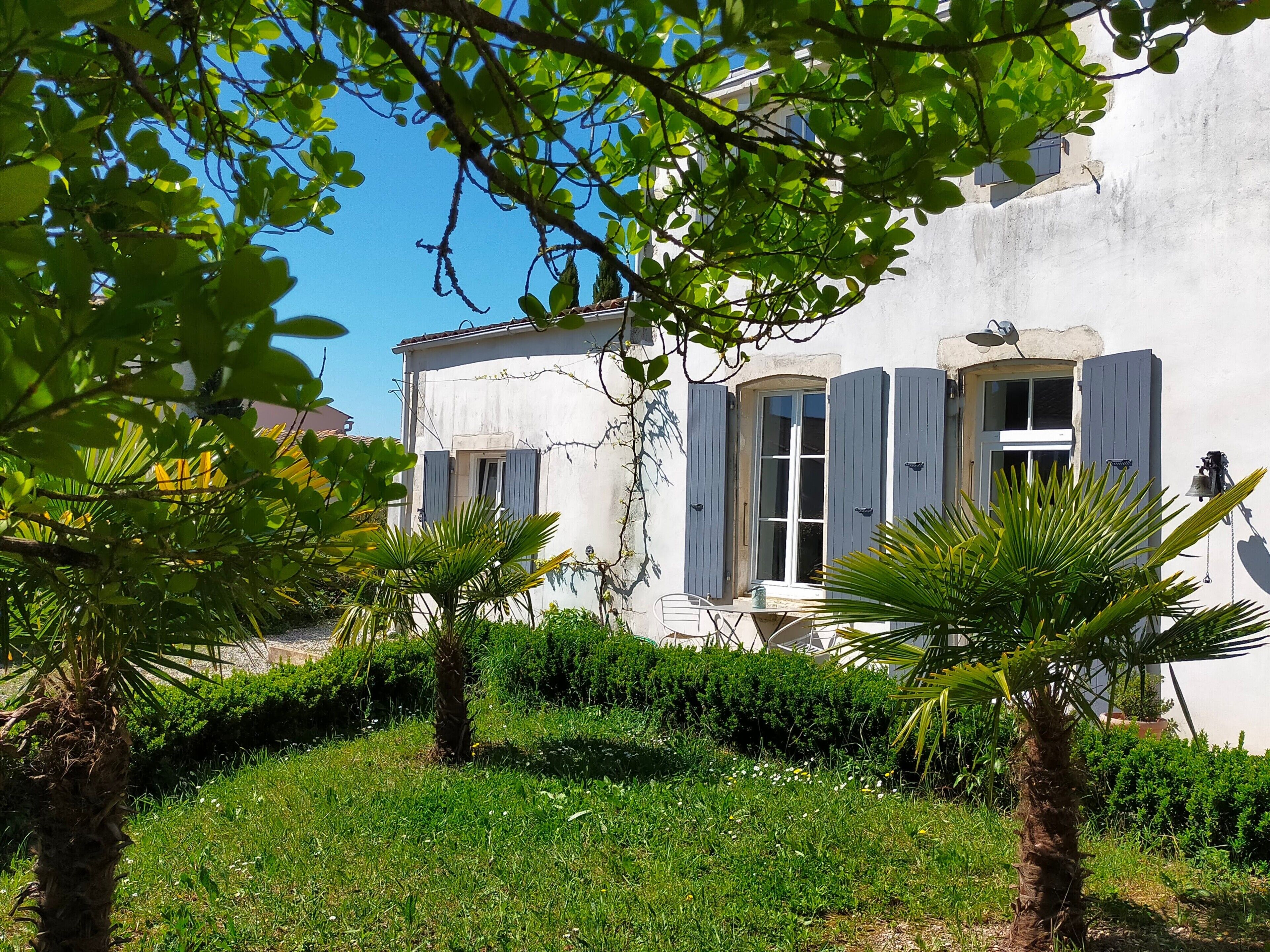 Un bâtiment à la façade blanche, aux volets bleus et doté d’un petit balcon avec une table et une chaise.
