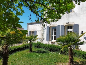 Un bâtiment à la façade blanche, aux volets bleus et doté d’un petit balcon avec une table et une chaise.