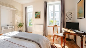 A bedroom with a bed, a desk, a chair, a potted plant, a radiator, and a window with curtains.