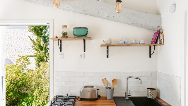 A kitchen with a gas stove, a toaster, a sink, and wooden shelves with kitchen items.