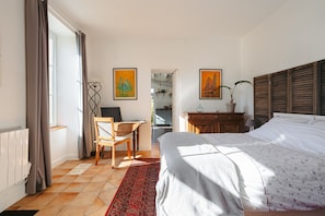 Ein Schlafzimmer mit Bett, Schreibtisch, Stuhl, Heizkörper und einem fensterbepflanzten Fenster.