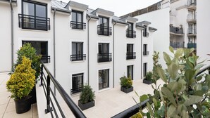 A modern multi-story residential building with balconies, potted plants, and a tiled courtyard. - LA VILLA Le Bourget Paris Parc des Expos (Le Bourget)